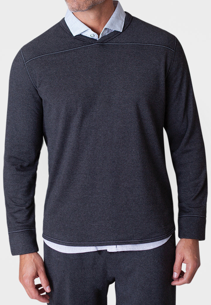 Man wearing a dark gray long-sleeve shirt over a light blue collared shirt on a white background